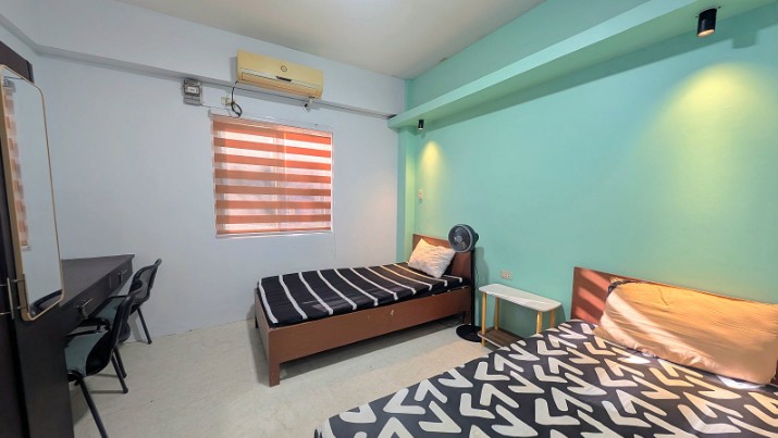 A dormitory room with mint walls, a desk and two beds