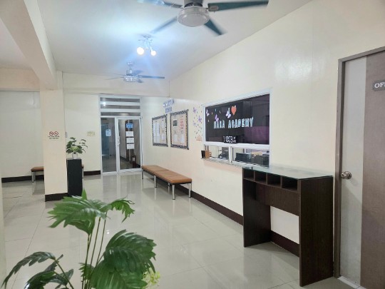 A tidy indoor space at HANA Academy with benches, notice boards and a potted plant