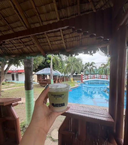 Tangan memegang minuman matcha di gazebo tepi kolam