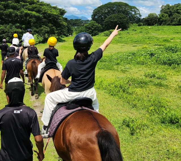 Anak-anak berhelm menunggang kuda di jalur yang melewati padang rumput