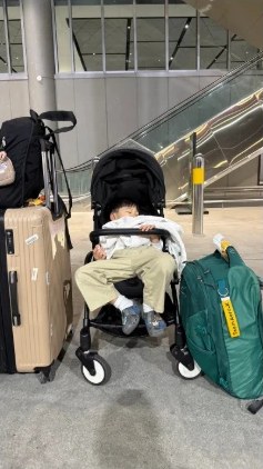 空港でスーツケースの横のベビーカーに座って眠る子ども