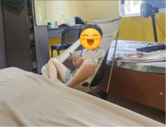 Seorang anak bersantai di kursi camping ringan di kamar asrama